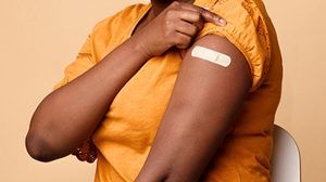 Woman holding sleeve up showing band-aid on arm after having a vaccination shot.