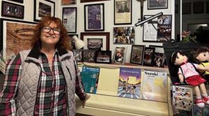 While giving Ashland.news a tour of her home violin studio, Ashland violinist and music teacher Faina Podolnaya poses among awards, concert flyers and photos of her students. Ashland.news photo by Sydney Seymour